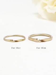 two gold wedding rings sitting on top of a white table next to a pink flower