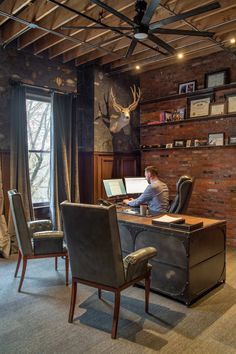 a man sitting at a desk in front of a brick wall with deer heads on it