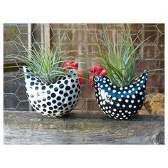 two ceramic chickens sitting next to each other on a wooden table with plants in them