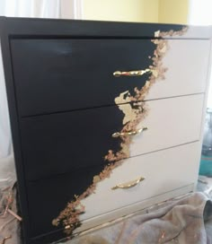 a black and white dresser with gold paint peeling off the top part of it's drawers