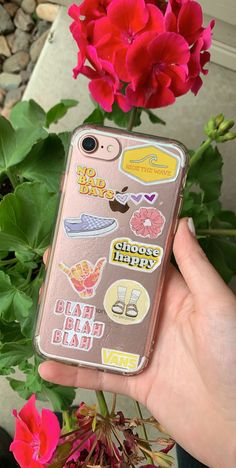 a person holding up a phone case with stickers on it and flowers in the background