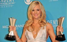 a woman holding two awards in her hands and posing for the camera with one hand