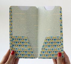 two hands holding an open book with blue and yellow designs on the pages, in front of a white background