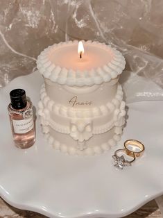 a wedding cake with two rings and a bottle of perfume on the table next to it