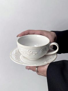 a person holding a white cup and saucer