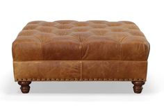 a brown leather ottoman with wooden legs and studding on the bottom, in front of a white background