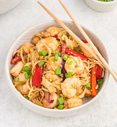 a white bowl filled with shrimp and vegetables next to chopsticks on the side