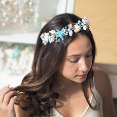 a woman with long hair wearing a blue flower headband and white tank top is looking down at her left shoulder