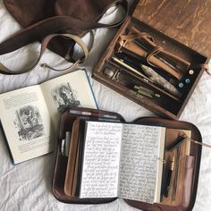 an open book and some writing utensils on a bed