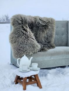 a gray couch sitting in the snow next to a white tea pot and saucer