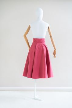 a mannequin wearing a pink skirt on a white display stand in front of a white wall