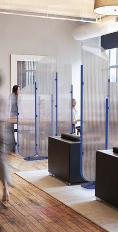 people are walking around in an office with privacy screens on the walls and wooden floors