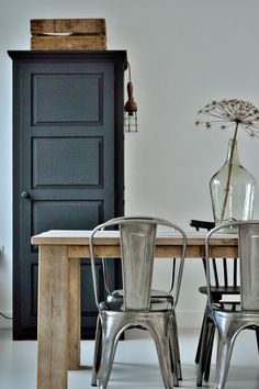 two metal chairs sitting at a wooden table in front of a black cabinet and door