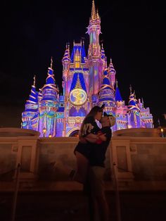 a man and woman kissing in front of a castle lit up with lights at night