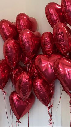 a bunch of red heart shaped balloons hanging on the wall