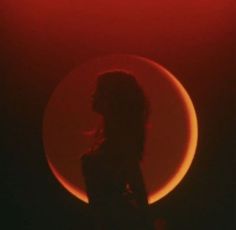 the silhouette of a woman in front of a red and black background with an orange circle