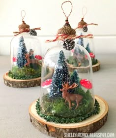 three glass cloches filled with miniature christmas trees and deer figurines on wood slices