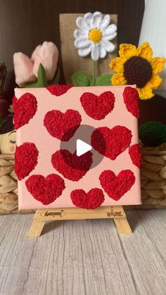 a red and pink painting with hearts on it, surrounded by flowers in the background