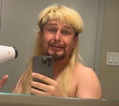 a man with long blonde hair is taking a selfie in front of a mirror