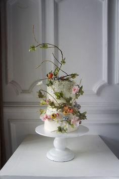 a three tiered cake with flowers and vines on top is sitting on a white pedestal