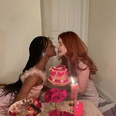 two women sitting at a table with a cake in front of them and one is kissing the other