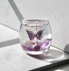 a glass vase filled with purple rocks and water on top of a white countertop