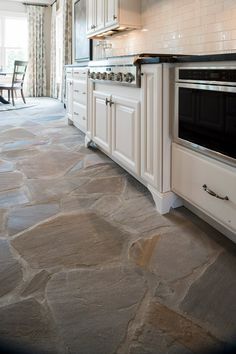 a kitchen with stone flooring and white cabinetry, stove top oven and dining room table in the background