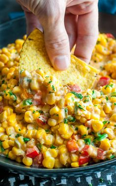 a person dipping a tortilla chip into a bowl filled with corn and salsa