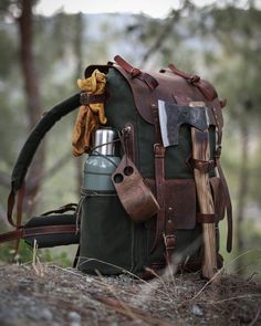 an old backpack with leather straps and tools attached to it sitting on the ground in front of some trees