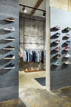 the inside of a clothing store with shoes on racks and clothes hanging up against the wall