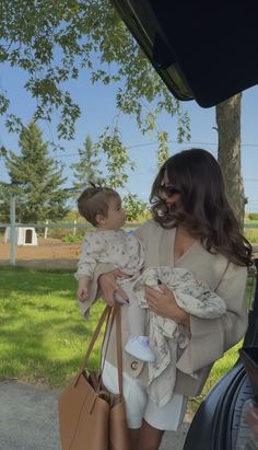 a woman holding a baby in her arms while standing next to a brown handbag