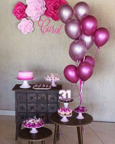 a table topped with lots of pink and purple balloons next to a wall mounted cake