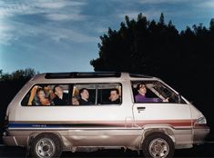 a group of people sitting in the driver's seat of a van with trees in the background