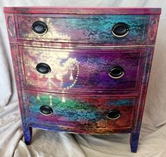 a multicolored chest of drawers sitting on top of a white sheet