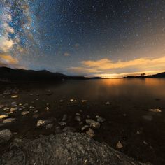 the night sky is filled with stars above water and rocks, as seen from an island