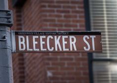 a street sign on a pole in front of a brick building with the word bleecker st painted on it