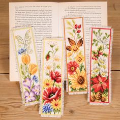 four cross stitch bookmarks with flowers and butterflies on them, sitting on a wooden surface