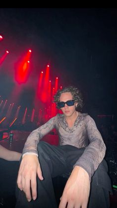 a man sitting on top of a chair in front of red and white lights at a concert