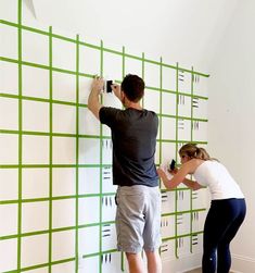 a man and woman standing next to each other in front of a wall with green squares on it