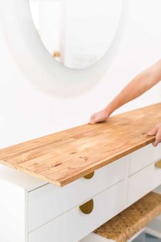 a person standing on top of a wooden counter next to a white dresser with drawers