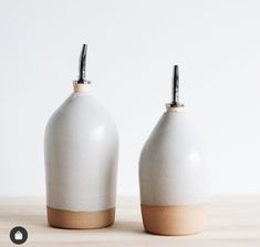 two white and brown vases sitting on top of a wooden table next to each other