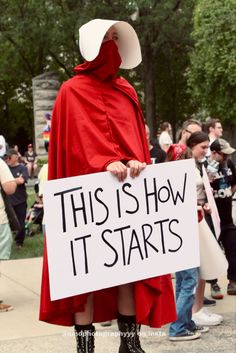 a person in a red cape holding a sign that says, this is how it starts