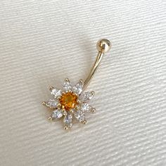 an orange and white diamond navel ring on a white surface with the top section being held up by a gold bar