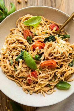 a white bowl filled with pasta and spinach on top of a wooden table next to a