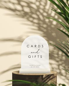 a white card and gifts sign sitting on top of a wooden stand next to a plant