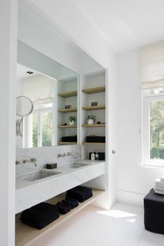 a white bathroom with two sinks and open shelves on the wall next to each other