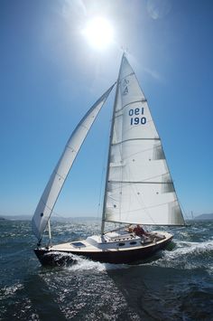 a sailboat is sailing on the water with sun shining in the sky behind it