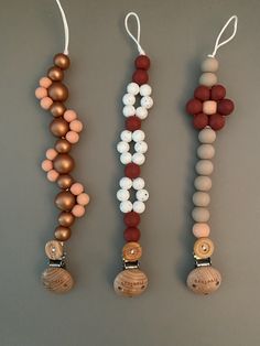 three wooden beaded necklaces hanging from strings on a gray surface with white and brown beads