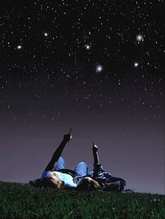 two people laying on the grass under stars in the night sky with their hands up