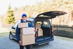 a man holding a box in front of his car with the back door open and moving boxes